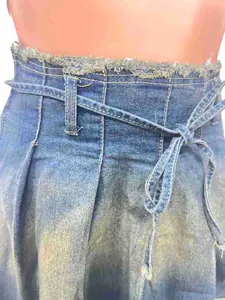 Detalle de la cintura de una falda plisada de mezclilla lavada con bordes deshilachados