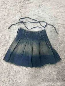 Primer plano de falda plisada vaquera lavada con efecto degradado y flecos largos.