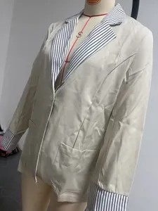 Detail shot of beige blazer featuring contrast black and white striped lapels and cuffs.