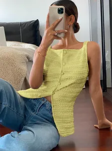 Woman wearing a yellow textured sleeveless button-up top with blue jeans.