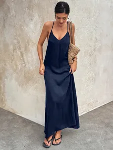 Model in a navy blue V-neck backless spaghetti strap maxi dress with casual summer straw bag