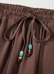 Detailed view of brown high-waisted wide-leg pants featuring a beaded drawstring tie.