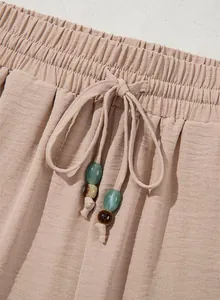 Detailed view of elastic waistband with beaded drawstring on loose casual pants
