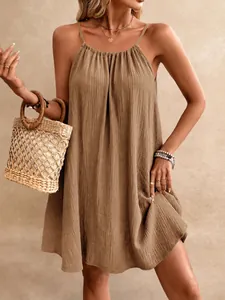 Détail d'une mini-robe dos nu marron en tissu froissé avec un sac en paille chic