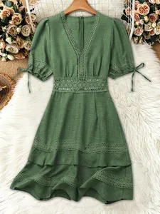 Primo piano del vestito verde con scollo a V, vita in pizzo e motivi floreali traforati