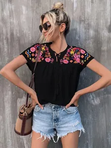 Close-up of black embroidered blouse with colorful geometric patterns and tassels.