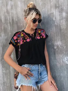 Detail of women's black embroidered blouse with tassel tie-neck and colorful patterns.