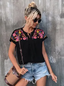 Detail of boho style embroidered black blouse with tassel tie neck for summer