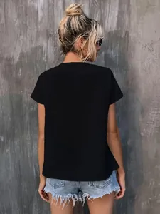 Back view of a casual black short-sleeve women's top styled with denim shorts against a gray wall