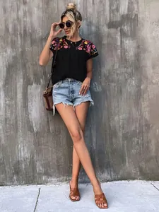 Bohemian style black blouse featuring colorful embroidery and tassels with denim shorts