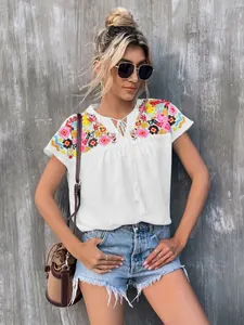 Close-up detail of white summer blouse featuring colorful embroidery and tie-neck with tassels