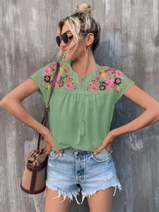 Detailed view of women's green blouse with vibrant embroidery and tassel neck ties