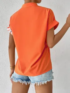 Vue arrière d'une chemise orange à manches courtes avec détails floraux aux poignets.