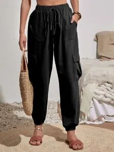 Detalle de los pantalones cargo negros con cordón, bolso de paja y sandalias planas
