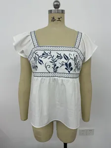 Detalle de una blusa de verano blanca con bordado floral azul y mangas con volantes