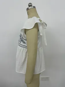 Detalle lateral de blusa blanca de verano con bordado azul y mangas de volantes