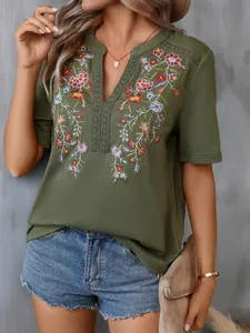 Detailed close-up of intricate floral embroidery and lace trim on a green V-neck summer blouse