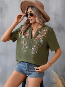Close-up detail of olive green blouse with floral embroidery and elegant lace trim.