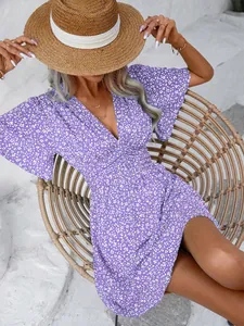 Close-up detail of a purple floral V-neck dress worn by a model sitting on a woven chair