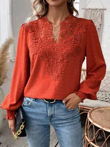 Close-up detail of stylish orange V-neck blouse featuring lace trim and swiss dot texture