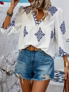Nahaufnahme einer eleganten weißen Damenbluse mit blauer Boho-Stickerei und V-Ausschnitt