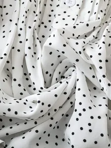 Nahaufnahme von weißem Chiffonstoff mit klassischem schwarzem Punktmuster und Knopf.
