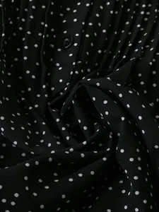 Nahaufnahme von schwarzem Polka-Dot-Chiffonstoff mit plissierter Textur und Knopf.