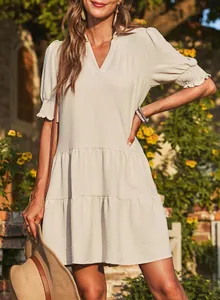 Detail of a beige tiered V-neck dress with ruffled sleeves in a sunny garden setting.
