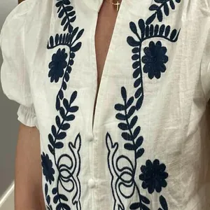 Détail de la broderie florale bleue sur une blouse en coton blanc à manches bouffantes