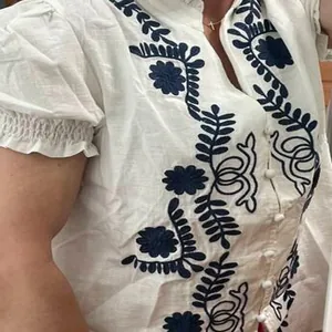 Détail d'un chemisier en coton blanc avec une broderie florale bleue complexe