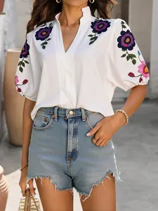 Vue détaillée d'une blouse blanche à col en V avec broderie florale sur les manches.