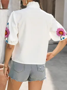 Vue arrière d'une blouse blanche avec col à volants et broderies florales roses