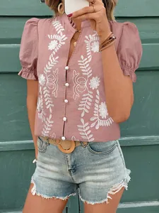 Détail d'une blouse en coton mauve brodée avec des boutons blancs et des motifs floraux.
