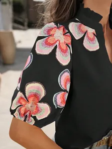 Gros plan sur le motif floral coloré des manches bouffantes d'un chemisier noir chic