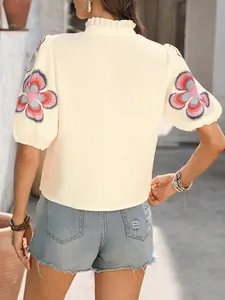 Détail du chemisier crème à col montant avec des broderies florales sur les manches.