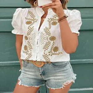 Gros plan d'un chemisier blanc en coton avec broderie dorée et manches bouffantes.