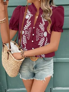 Détail d'une chemise en coton rouge vin avec broderie florale blanche et manches bouffantes