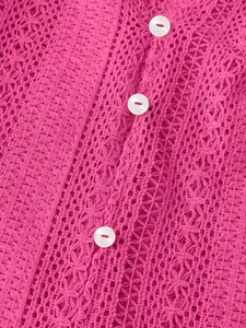 Gros plan sur un tissu en dentelle ajourée rose avec des boutons blancs sur un haut.