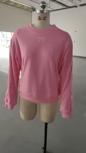 Primo piano della felpa rosa girocollo con ricamo a fiocco bianco su un manichino sartoriale