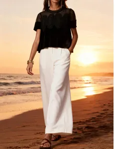 Model in black velvet mesh lace top and white wide-leg trousers on beach sunset