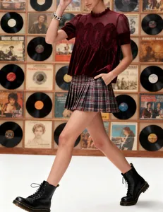 Model wearing a burgundy velvet top with mesh lace details and a plaid pleated skirt