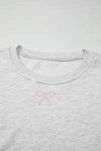 Dettaglio del ricamo a fiocco rosa sulla scollatura di un pullover in cotone grigio