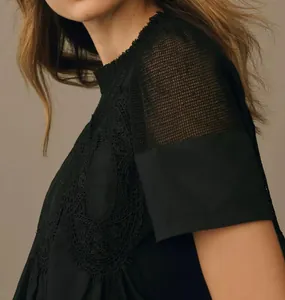 Gros plan d'un haut noir avec broderie en dentelle et détail d'épaule en maille.