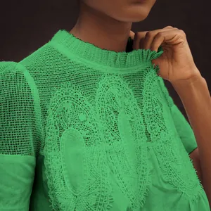 Détail d'un haut vert en dentelle brodée avec col rond à volants et manches en résille.