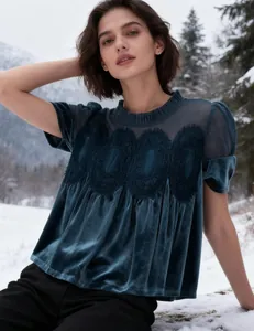 Detailed view of dark teal velvet top with mesh panel and embroidery on a model in snow.
