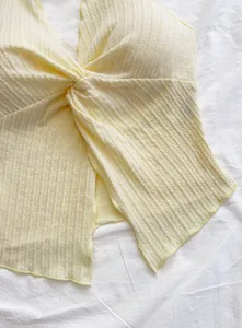 Detail view of a light yellow ribbed halter neck crop top with a stylish twist-front design