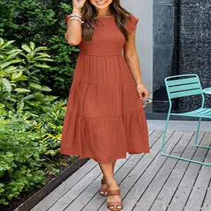 Full view of rust red tiered midi dress with flutter sleeves in garden setting
