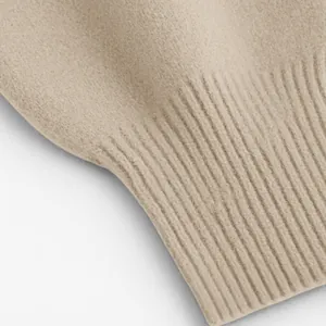 Detailaufnahme der weichen, gerippten Manschettentextur eines beigen Strickpullovers