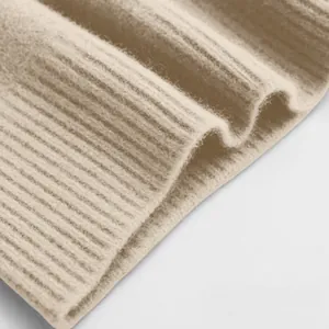 Nahaufnahme der beigefarbenen Rippstrick-Stoffstruktur eines weichen Herbst-Winter-Pullovers.