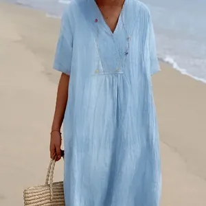 Detail of light blue V-neck maxi dress with loose fit and textured fabric on the beach